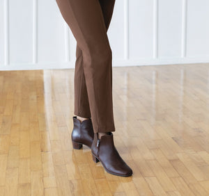 Landyn ankle boot in brown leather with outside zipper on model in brown slacks in open space with wood floor and white wall.